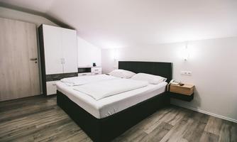 A modern bedroom with a large bed and wooden floor. There is a wardrobe and nightstands against the walls.