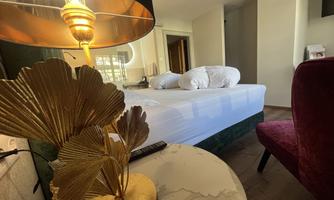 A stylish hotel room with a large bed and soft pillows. On the table, there is a decorative lamp and an elegant table decoration.