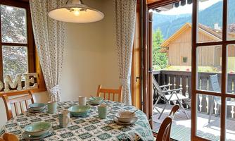 A cozy dining area with a table set for breakfast. A view of the surrounding mountains and a balcony through the windows.