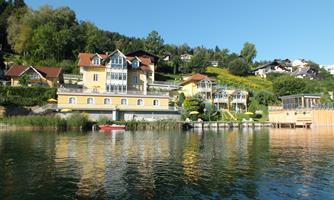 A tranquil lake with beautiful yellow holiday homes by the shore. In the background, green hills and trees can be seen.