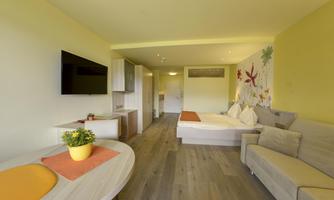 A modern room with a double bed, a television, and a cozy sofa. The walls are friendly in yellow and decorated with colorful flowers.