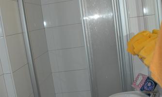 A small bathroom with a shower cubicle and a sink. Towels in various colors are lying on the shower wall.