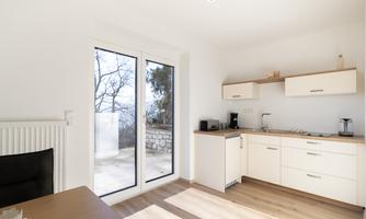 A bright and modern kitchen corner with white furniture and wooden details. Large windows provide a view and plenty of natural light.
