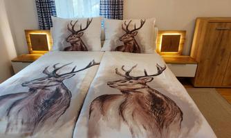 A modern bedroom with a double bed and bedding featuring a deer motif. The decor is bright and cozy, with warm wood and soft lighting.