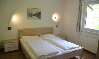 A simple bedroom with a double bed and two nightstands. A picture hangs on the wall, and a window provides natural light.