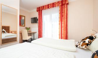 A bright bedroom with a large window and red curtains. The room is furnished in a modern style, with a mirror, a table, and a television.