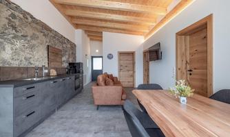 A modern kitchen with wooden ceilings and an open living area. The furniture is simple and elegant, featuring a cozy dining table and a seating area.