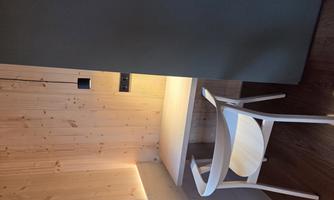 A modern workspace with a bright desk and a white chair. The walls are made of wood, and there is soft lighting.