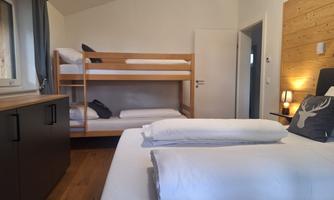 The pleasantly designed bedroom offers thoughtful comfort for families or small groups. In addition to a spacious double bed with stylish decorative pillows and warm wood panelling on the wall, there is a practical bunk bed – ideal for children or additional guests. Light wood floors, subtle lighting and soft colours create a pleasant, calm atmosphere. A window provides natural light, while ample storage space is available in the wardrobes.’