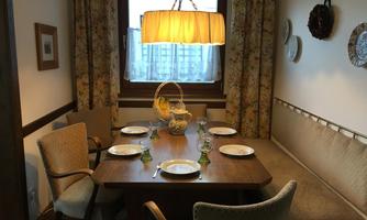 A cozy dining area with a wooden table and chairs. A bright light and decorative curtains create an inviting atmosphere.