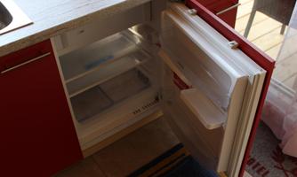 An open refrigerator in a modern kitchen with red cabinets. The shelves are empty and the refrigerator has a clear, immaculate interior.
