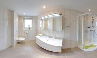 A modern bathroom with a bright tiled floor and large mirrors. The shower is partitioned and there is plenty of daylight through the window.