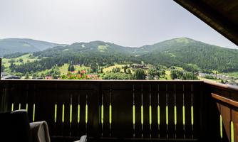 A balcony overlooking a green mountain landscape. The sun is shining and the surroundings are calm and peaceful.