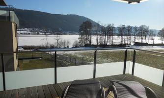 A balcony with two loungers and a view of a frozen lake. In the background, mountains and snow-covered meadows can be seen.