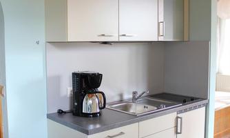 A modern kitchen with bright cabinets and a sink. On the countertop, there is a coffee machine and a vase with flowers.