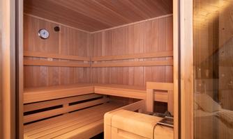 A cozy sauna room with wood paneling and benches. The temperature display is visible on the wall.