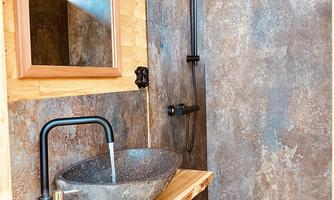 A modern bathroom with a stone washbasin and an elegant shower. The walls are made of stylish material, and there is a large mirror.
