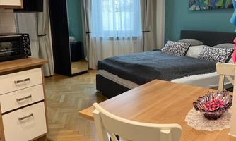 A cozy room with a bed, table, and chairs. Large windows let in a lot of light.