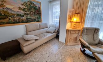 A cozy living space with a beige sofa and cushions. Next to the sofa stands a lamp and a comfortable armchair.