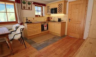 A bright kitchen with wooden furniture and a large window. The floor is made of wood and a dining table with chairs complements the space.