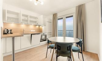 A modern kitchen with a round table and chairs. Large windows with a view of the surroundings and bright, neutral colors.