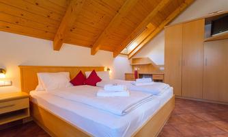A cozy bedroom with a double bed and red pillows. The room has a wooden ceiling and plenty of natural light.
