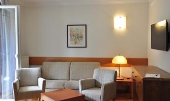 A modern living room with a bright sofa and two armchairs. A table and a television are also present, as well as a window with a balcony.