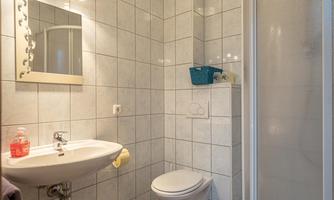 A modern bathroom with bright tiles and a shower. There is a sink and a toilet, which are functionally arranged.
