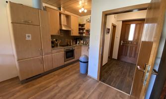 A modern kitchen with wooden cabinets and a stove. In the background, an open door is visible, leading to a hallway.