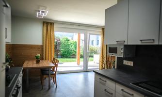 A modern kitchen with a dining area and a view of the garden. Large windows let in a lot of light.