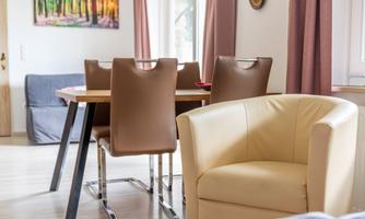Large wooden table with comfortable chairs and a cozy cocktail chair. Perfect for long game nights, shared meals, or a cup of tea with a view of the greenery.
