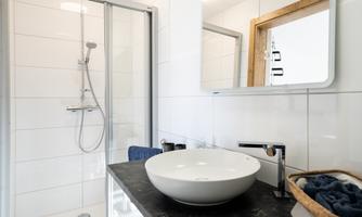 A modern bathroom with a shower enclosure and an elegant sink. The walls are brightly tiled, and the mirror adds a stylish accent.