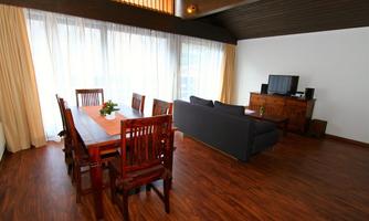 A modern living room with a wooden dining table and comfortable seating. Large windows provide plenty of natural light.