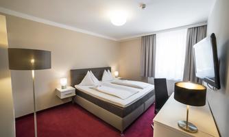 A modern bedroom with a double bed and a cozy decor. The room has bright walls and large windows that provide plenty of daylight.