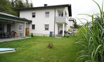 A modern house with two floors in a quiet environment. The garden is green and well-maintained, with a small flower in the middle.