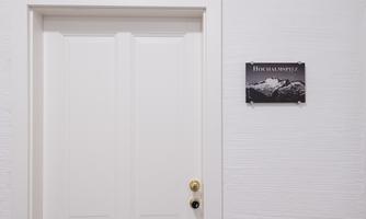A white door with a golden doorknob. Next to the door is a sign reading "Hochalmspitz".