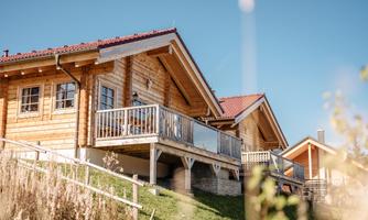 A charming wooden house with a large balcony and a red roof. The surroundings are green and invite relaxation.