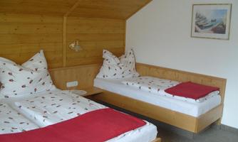 A simple room with two beds and natural wood paneling. The beds are decorated with red blankets and pillows.