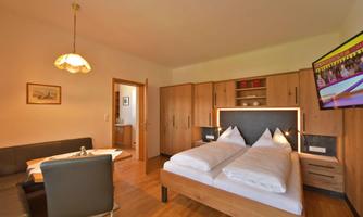 A cozy room with a double bed, wooden furniture, and a flat-screen TV. There is also a dining area with a seating group and table.