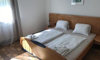 A simple bedroom with a double bed and two pillows. The room is bright, with natural light, and has a calm atmosphere.