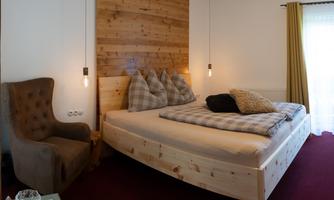 A modern bedroom with a wooden paneled wall and a cozy atmosphere. There is a large bed, pillows, and a comfortable armchair.