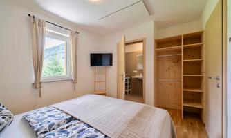 A bright bedroom with a double bed and modern decorations. A television and an open wardrobe are also available.