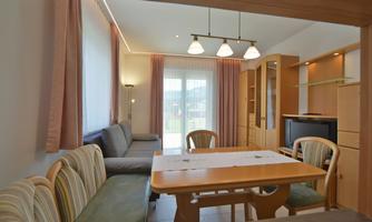 A bright living area with a dining table and a comfortable seating corner. Large windows provide plenty of daylight.