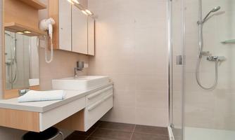 A modern bathroom with a bright design. It includes a shower, a sink, and a large mirror.