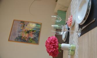 A stylishly set table with white plates and wine glasses. A vase with pink hydrangeas and a painted picture adorn the room.