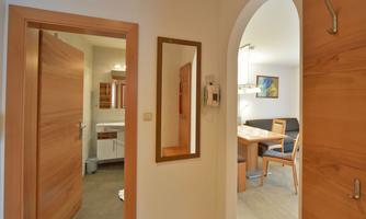 A bright hallway with wooden frames and a large mirror. In the background, there is a dining area with a table and chairs visible.