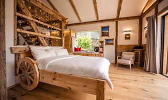 A cozy bedroom with a wooden bed and rustic decor. Large windows provide plenty of daylight and a view of the outdoors.