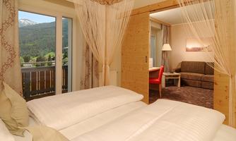 A stylish hotel room with a cozy double bed and a view of the mountains. The living area is modernly furnished and offers plenty of space to relax.
