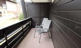A balcony with two gray chairs and a dark wall. The surroundings are green and quiet.