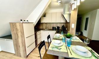 A modern kitchen with bright furniture and a dining table set for a meal. There are stylish glassware and fresh plants decorated.